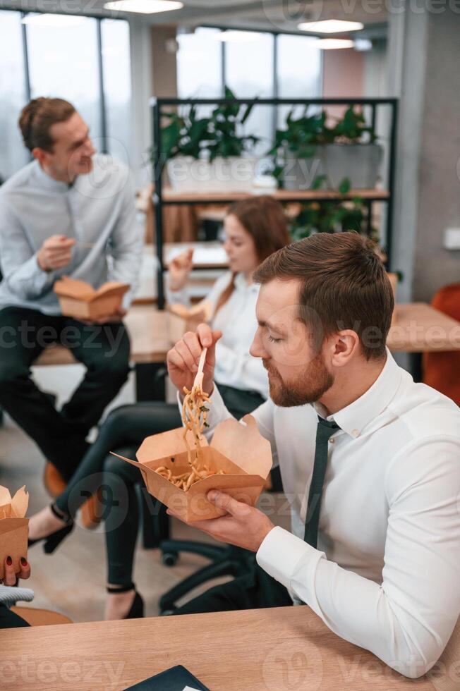 Having a conversation... Group of coworkers are eating food from eco boxes in the office together photo