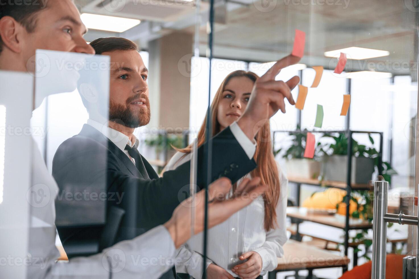 Plans for the project.. Group of coworkers in the office is standing together and putting stickers on the glass photo