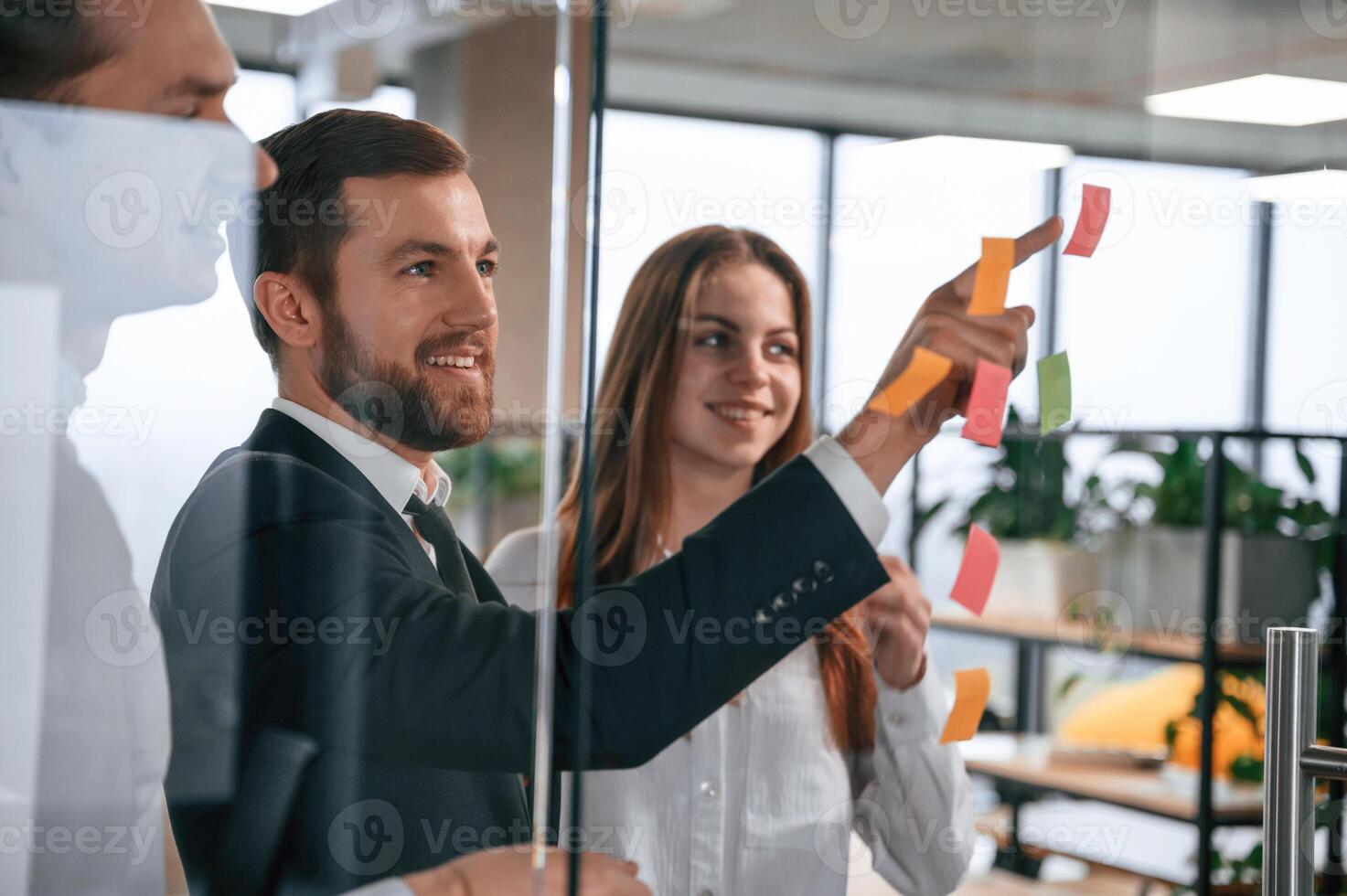 Plans for ,the project. Group of coworkers in the office is standing together and putting stickers on the glass photo