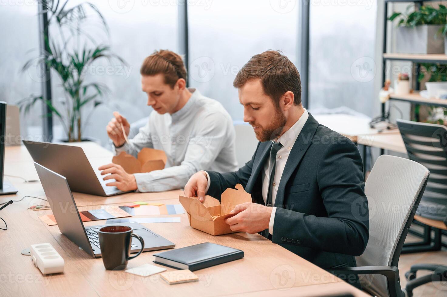 Two ,coworkers are eating food that is in the eco boxes. Sitting in the office photo