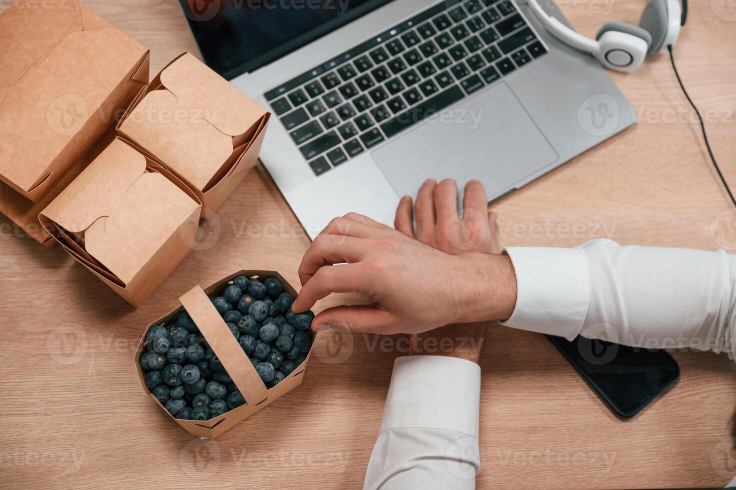 Taking blueberries.. Top view of hands of the man that is working by using laptop. Eco boxes with food photo