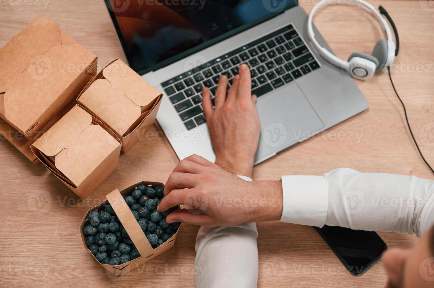 Taking blueberries. Top view of hands, of the man that is working by using laptop. Eco boxes with food photo