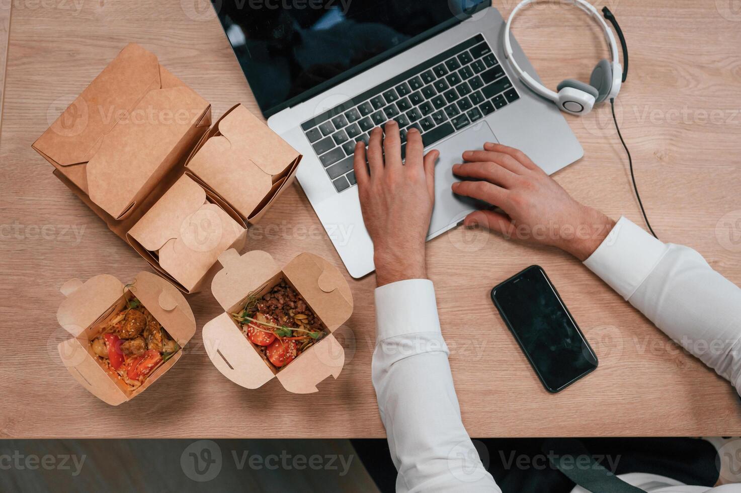 Top view ,of man's hands that is typing on the laptop. Food in the paper eco boxes are on the table photo