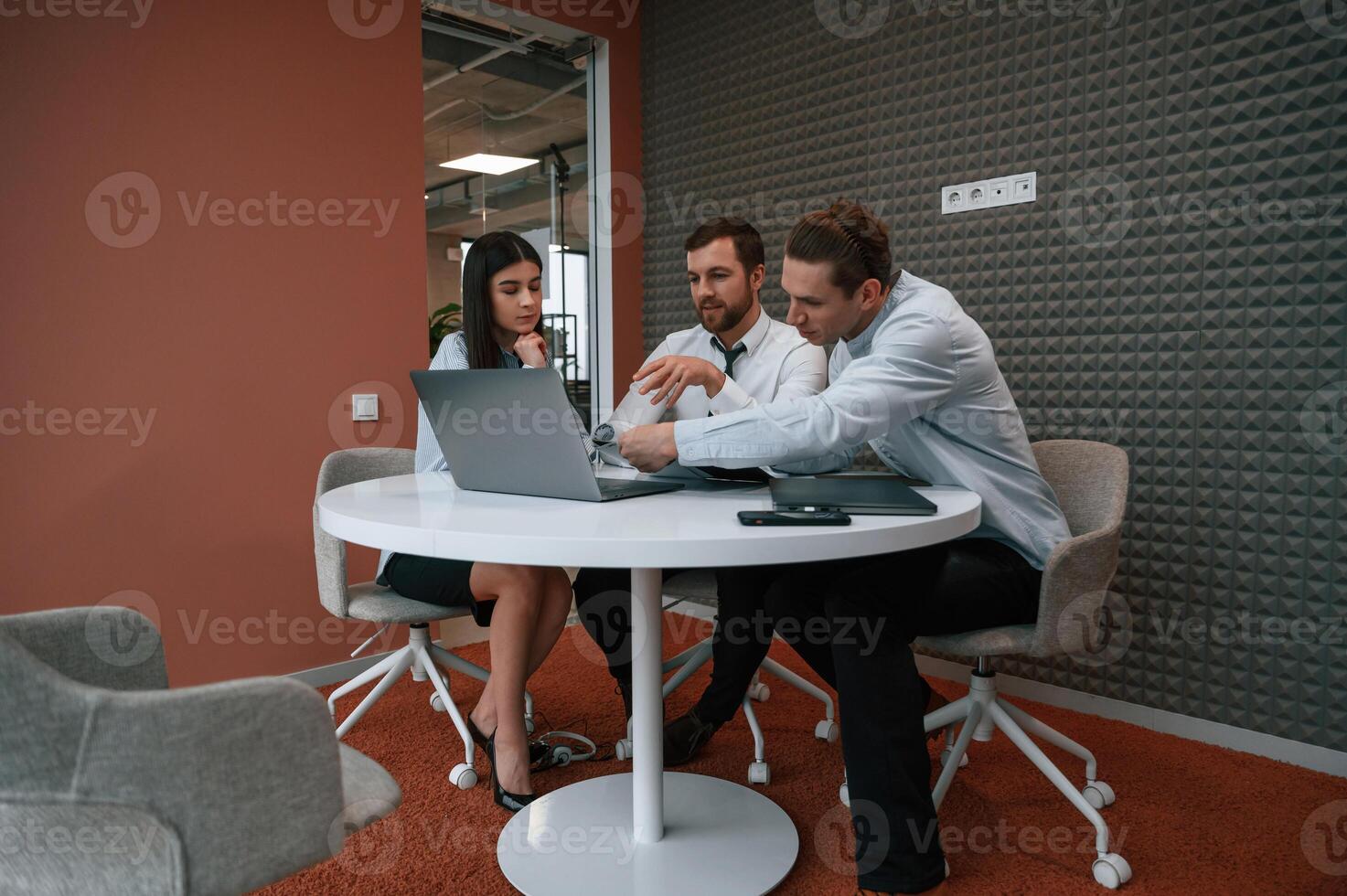 Sitting, talking, using laptop. Office workers are indoors .by the table photo