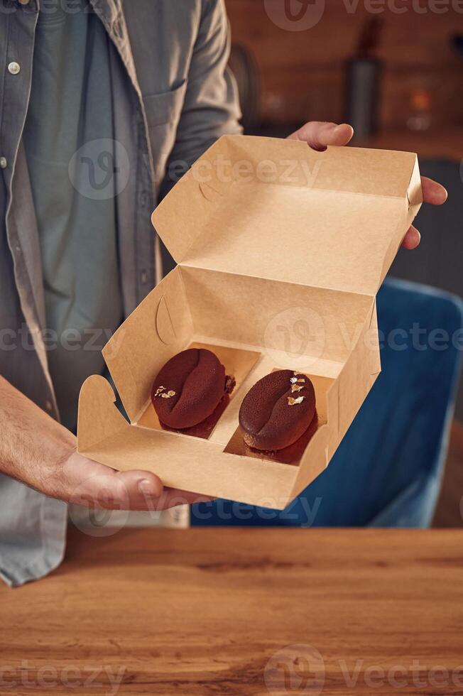 Coffee like look, design of the sweets. Man is with delicious desserts that are in the eco boxes. Standing indoors photo