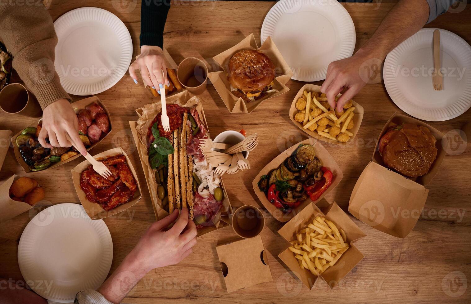 Top view of table with ,food on, it, hands of the people taking it, eating. Meat, vegetables, French fries, burger, mushrooms photo
