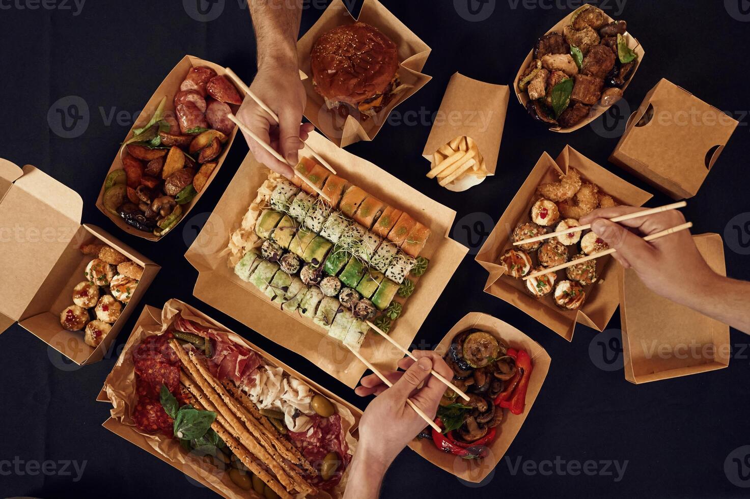 Top, view ,of table with food on it, hands of the people taking it, eating. Meat, sushi, vegetables, French fries, burger, mushrooms photo