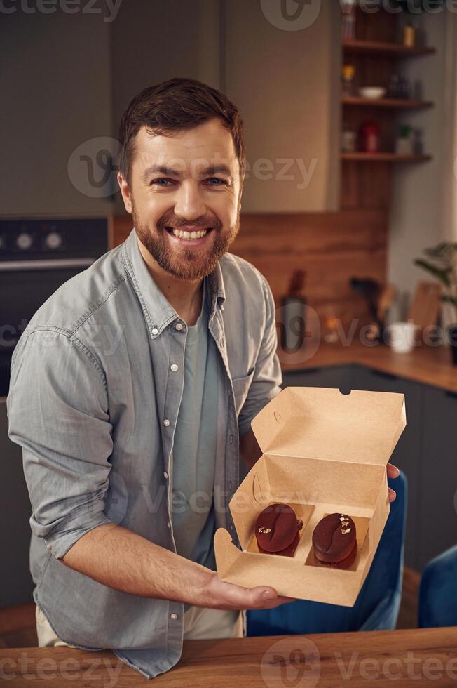Coffee like look, design of the sweets. Man, is with delicious desserts that are in the eco boxes. Standing indoors photo