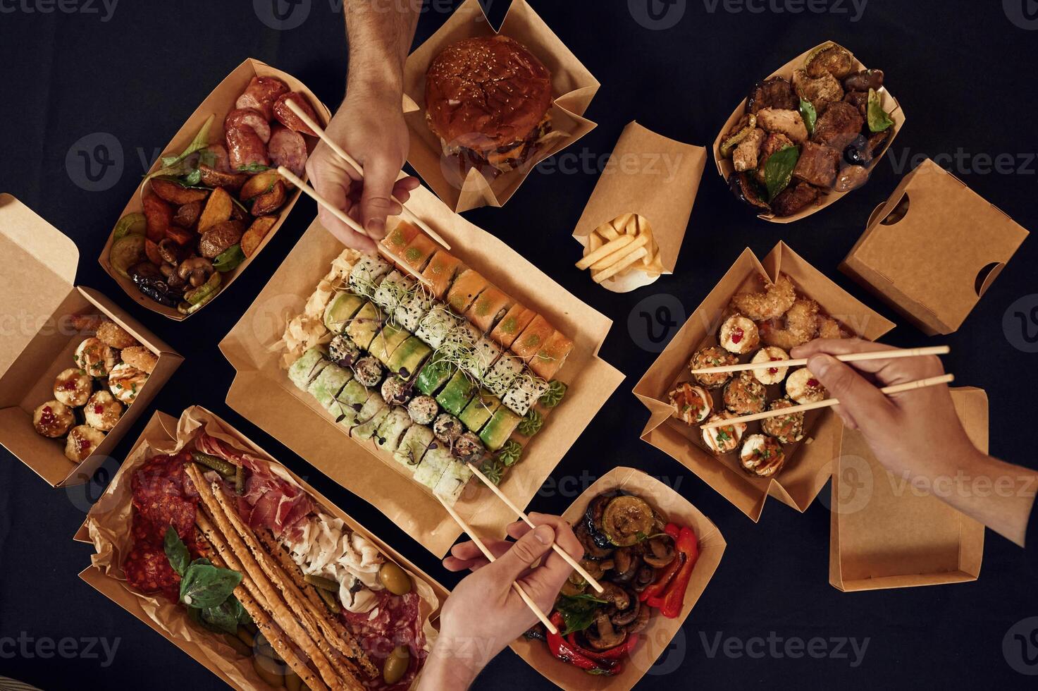 Top view of table with, food ,on it, hands of the people taking it, eating. Meat, sushi, vegetables, French fries, burger, mushrooms photo
