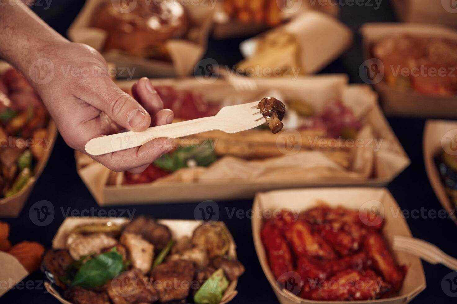 Man is holding ,fork with mushroom. Close up view of table with food on it. Meat, vegetables photo