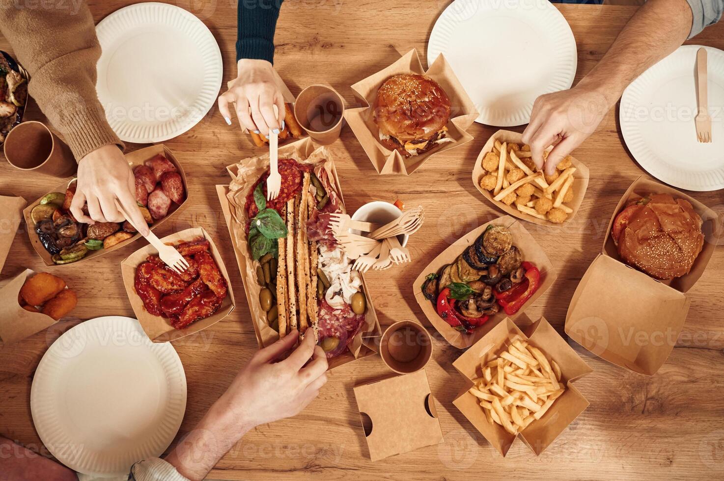 Top view of table with food on it, hands ,of the people taking it, eating. Meat, vegetables, French fries, burger, mushrooms photo