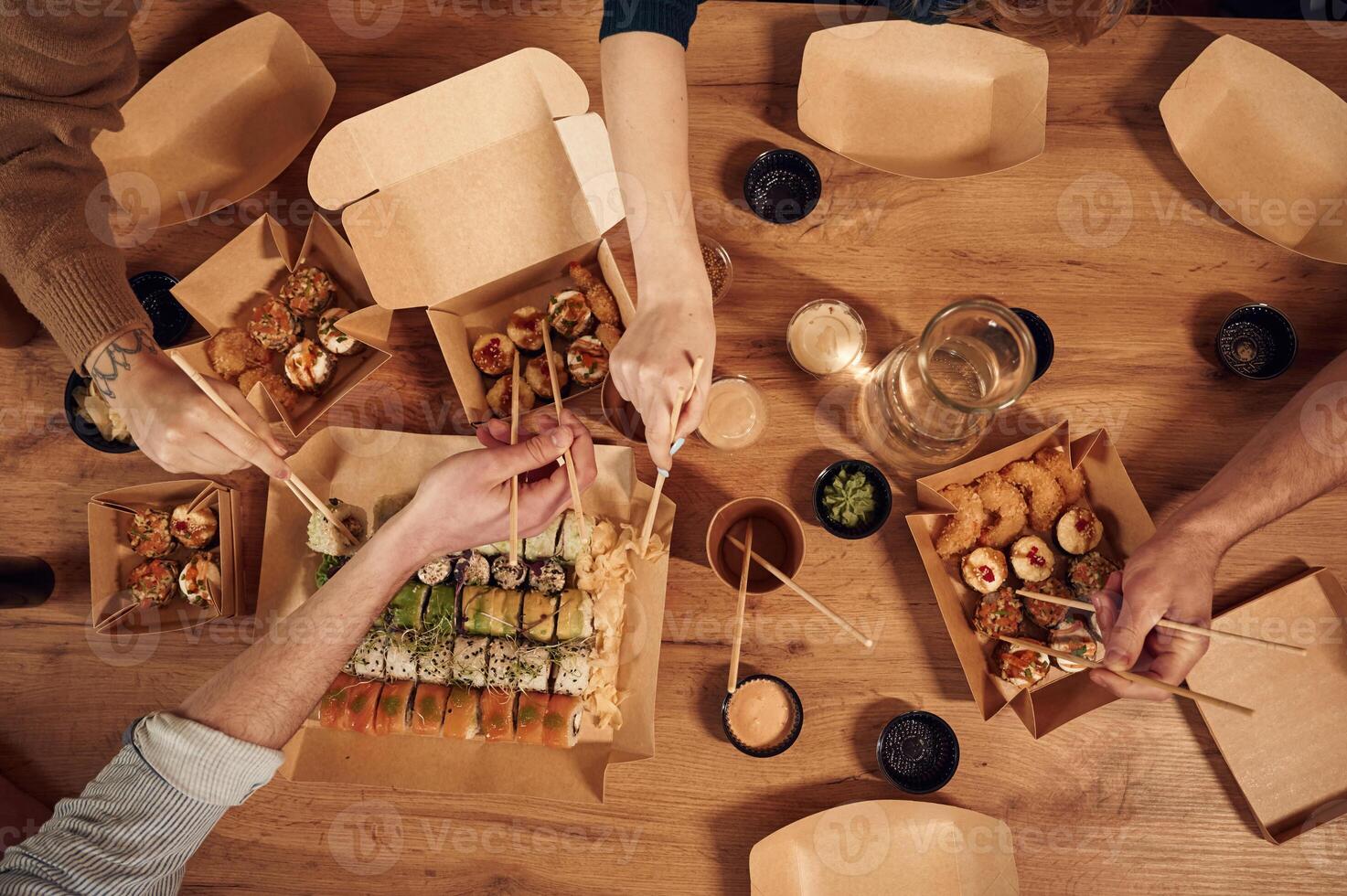 Top view ,of table with sushi on it in paper eco boxes, hands of the people taking it, eating photo