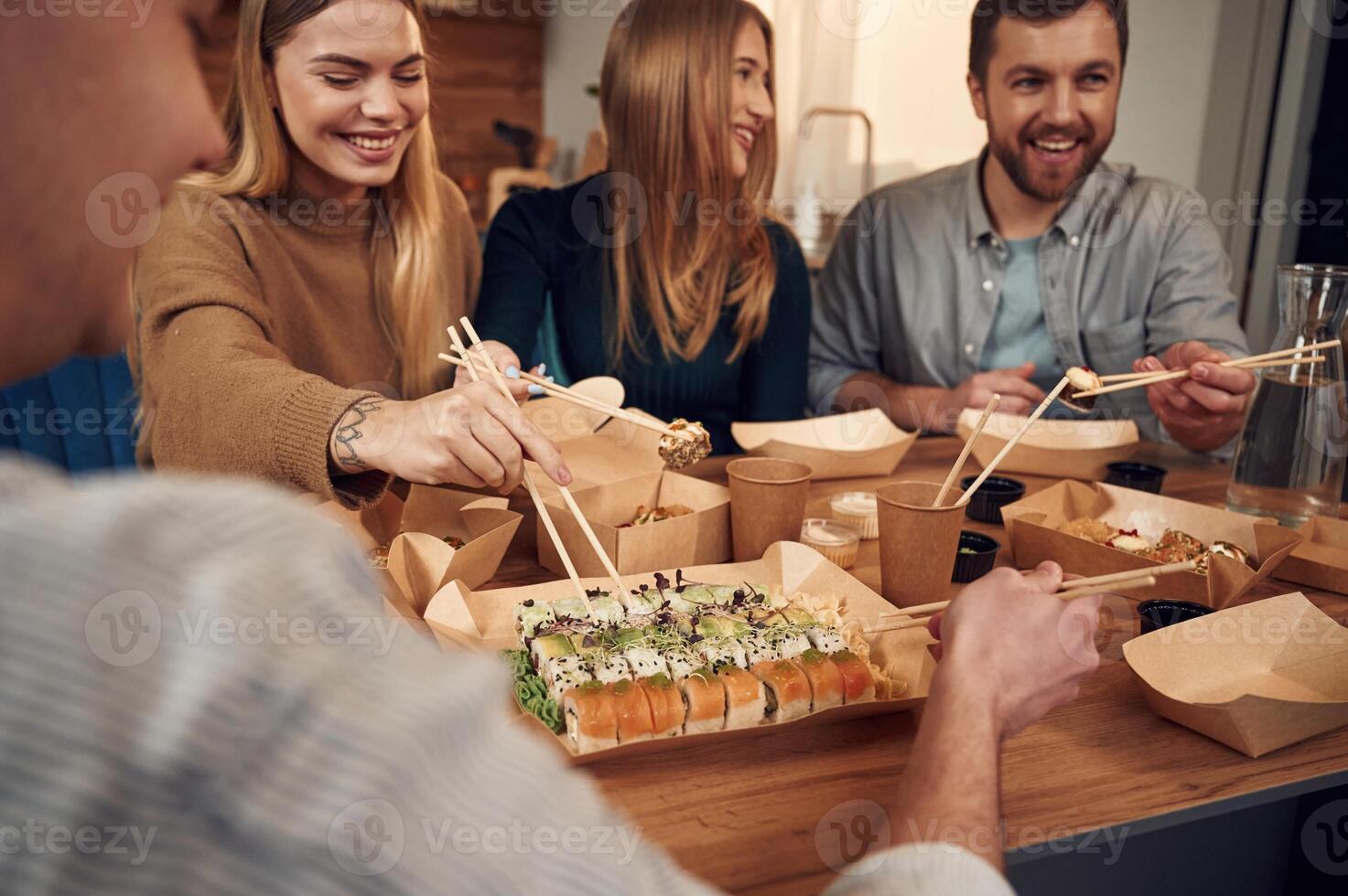 Using ,chopsticks. .Friends are sitting indoors at home and eating sushi together photo