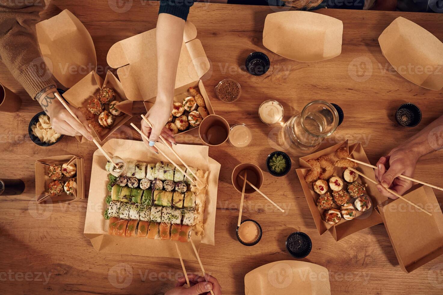 Top ,view of table with sushi on it in paper eco boxes, hands of the people taking it, eating photo