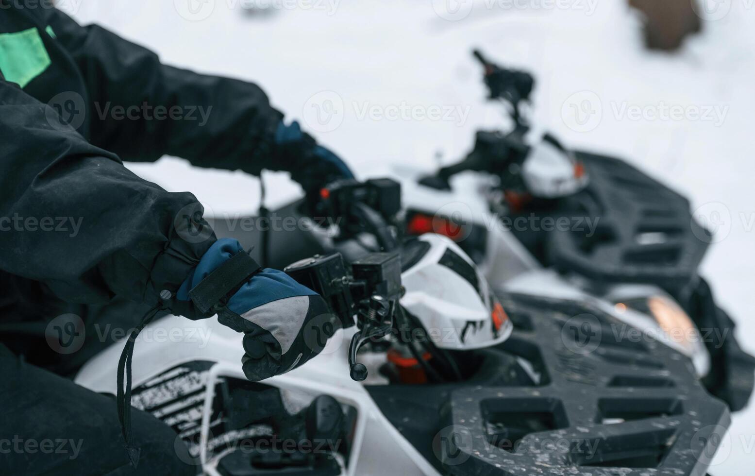 Close up view of the hands and front part of vehicle. Man is riding ATV outdoors in the winter forest photo