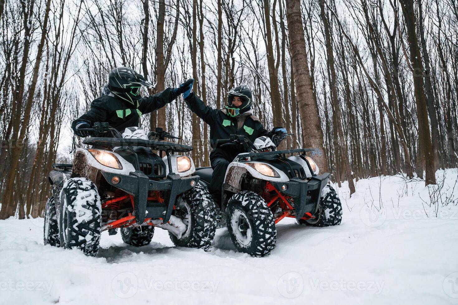 Making high five. Two people are riding ATV in the winter forest photo