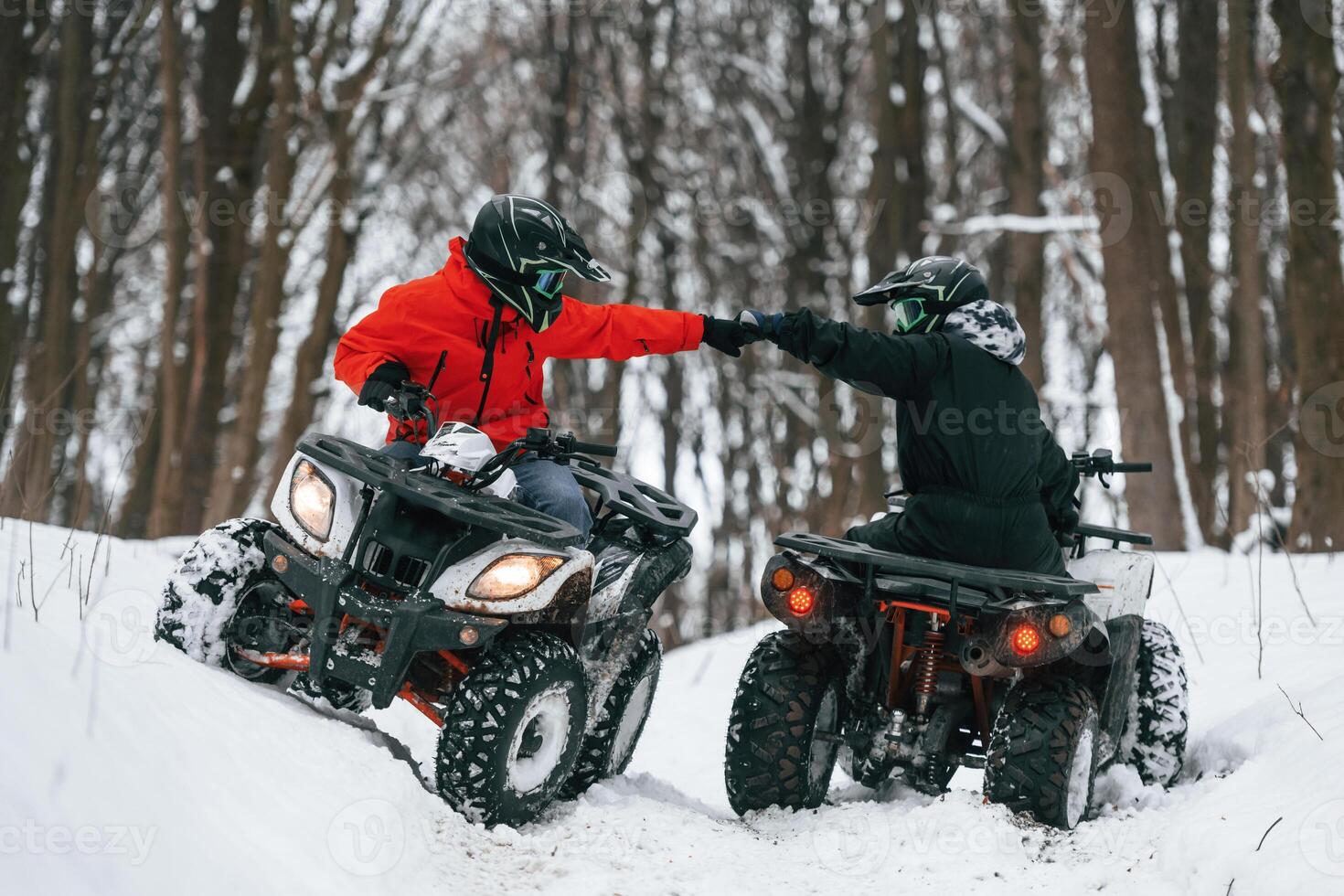 Knocking the, fists. Two people are riding ATV in the winter forest photo