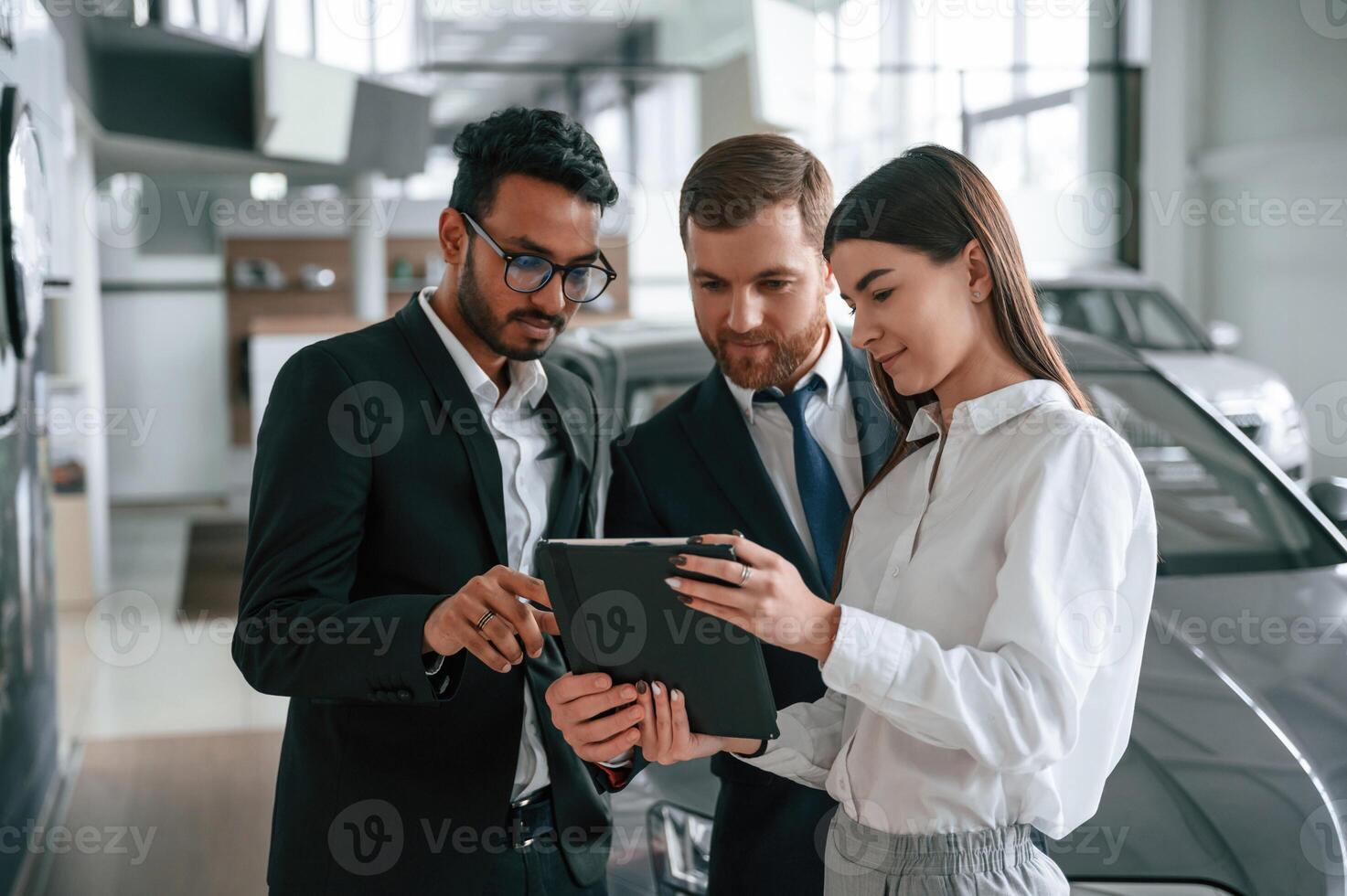 Standing and reading information in the graphic tablet. Three people are working together in the car showroom photo
