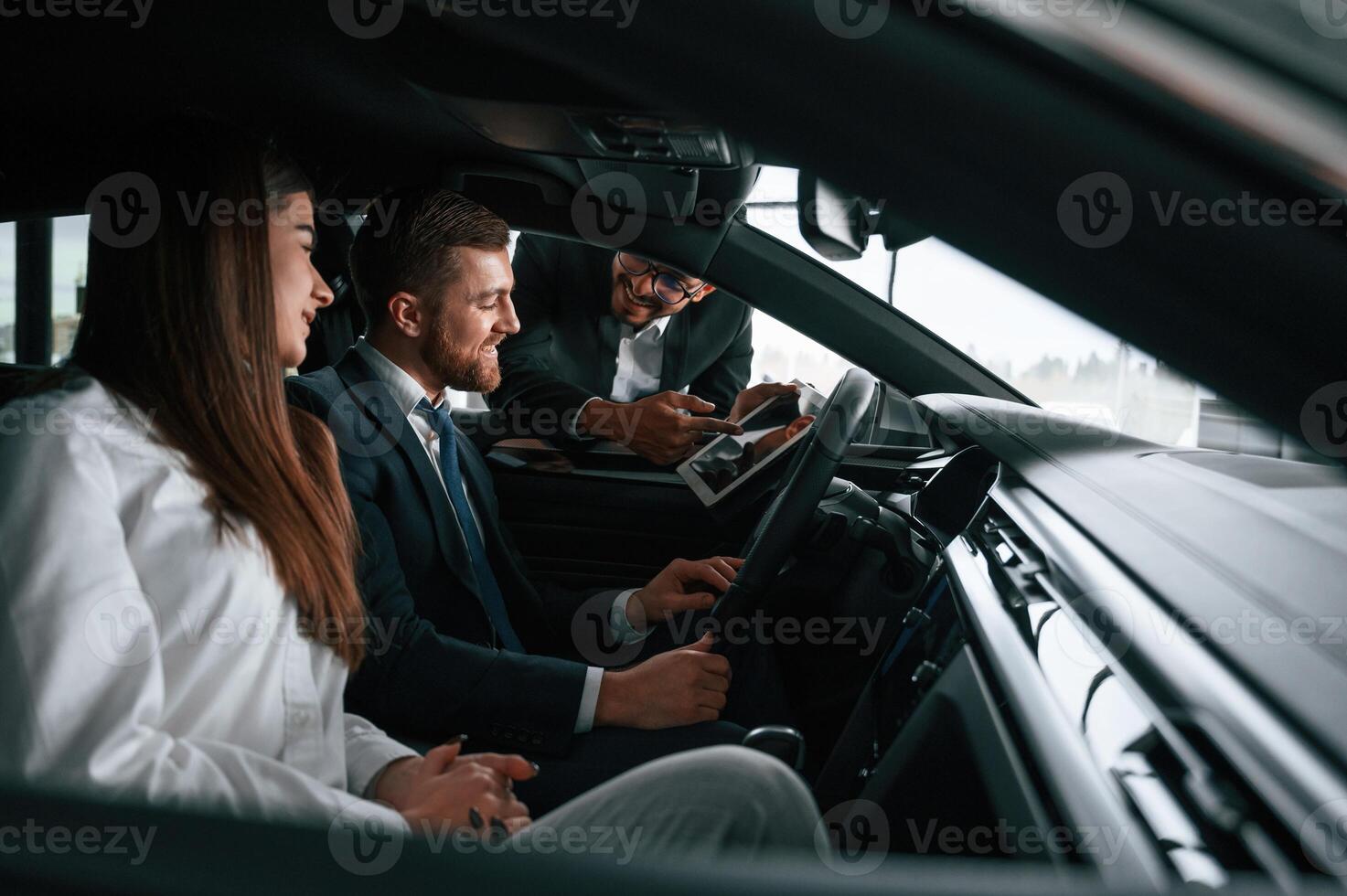 Car showroom ,worker is consulting man and woman that are sitting inside of automobile photo