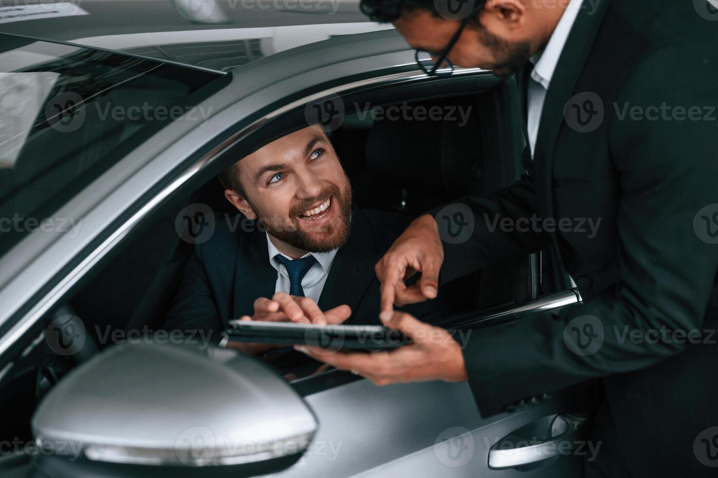 Man is sitting in the new automobile, consultant is showing details and data on graphic tablet to customer photo