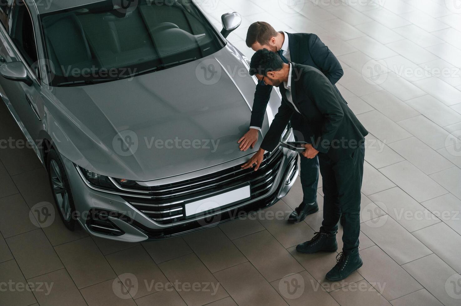 Checking the surface of gray automobile.. Two businessmen are working together in the car showroom photo
