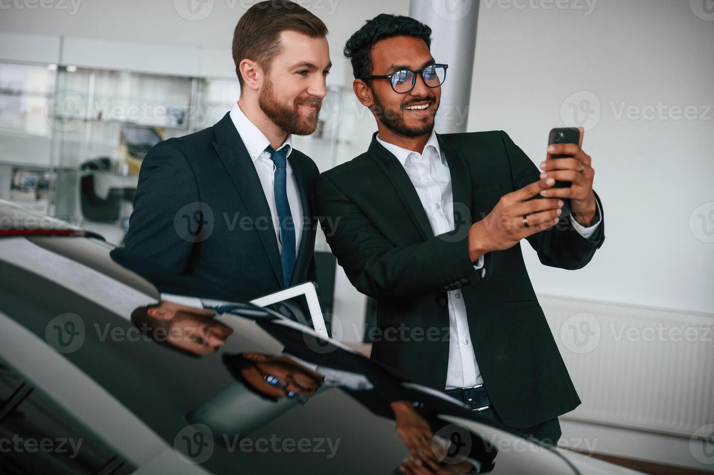 Having fun, using smartphone. Two businessmen are working together in the car showroom photo