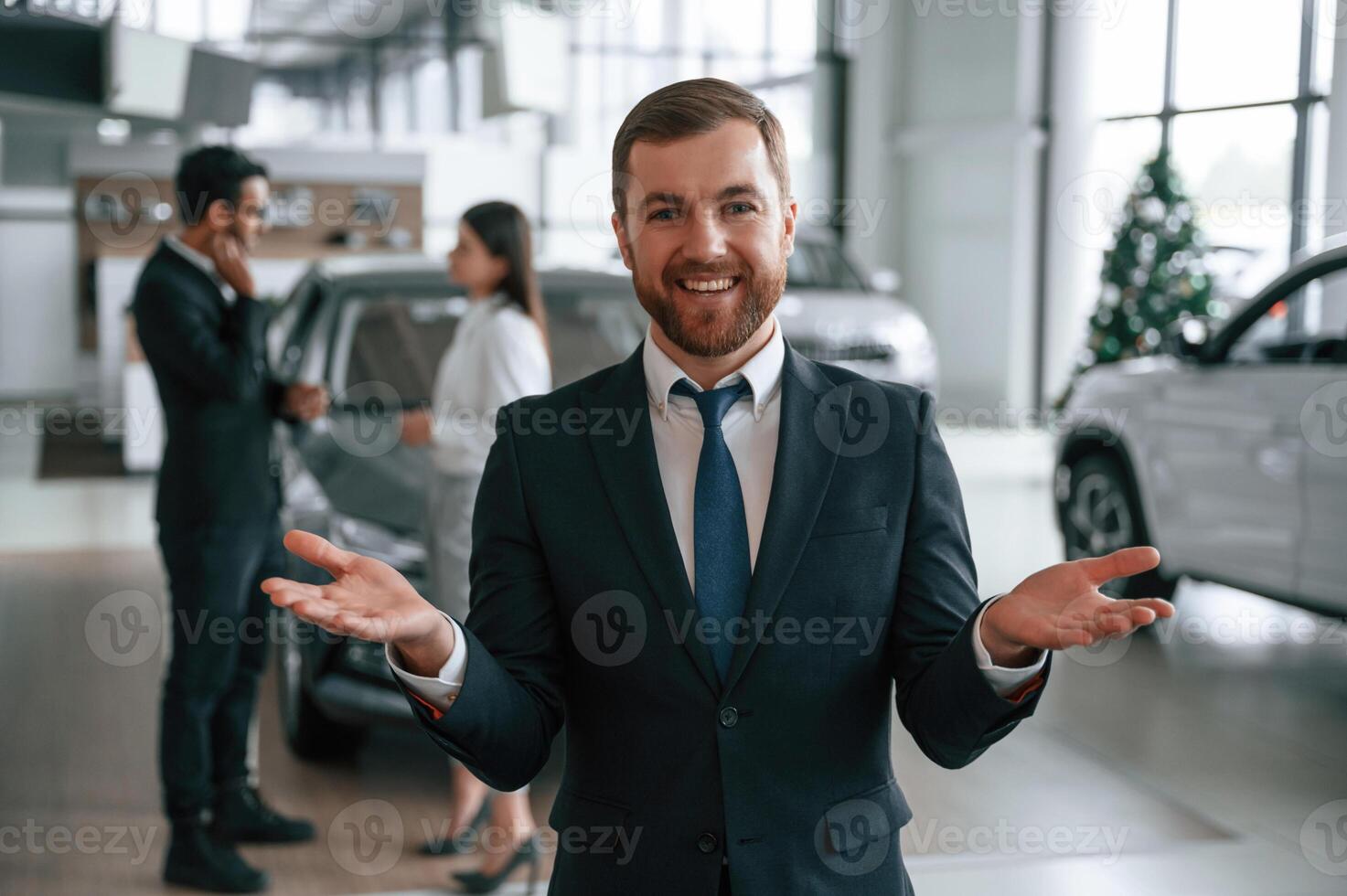 Handsome, man is standing in front of his coworkers. Three people are together in the car showroom photo