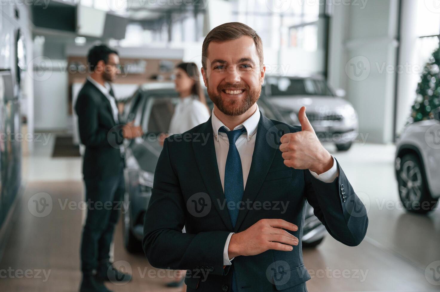 Handsome man ,is standing ,in front of his coworkers. Three people are together in the car showroom photo