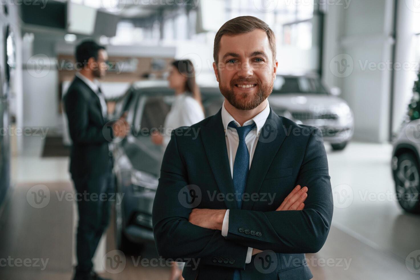 Handsome, man is standing ,in front of his coworkers. Three people are together in the car showroom photo