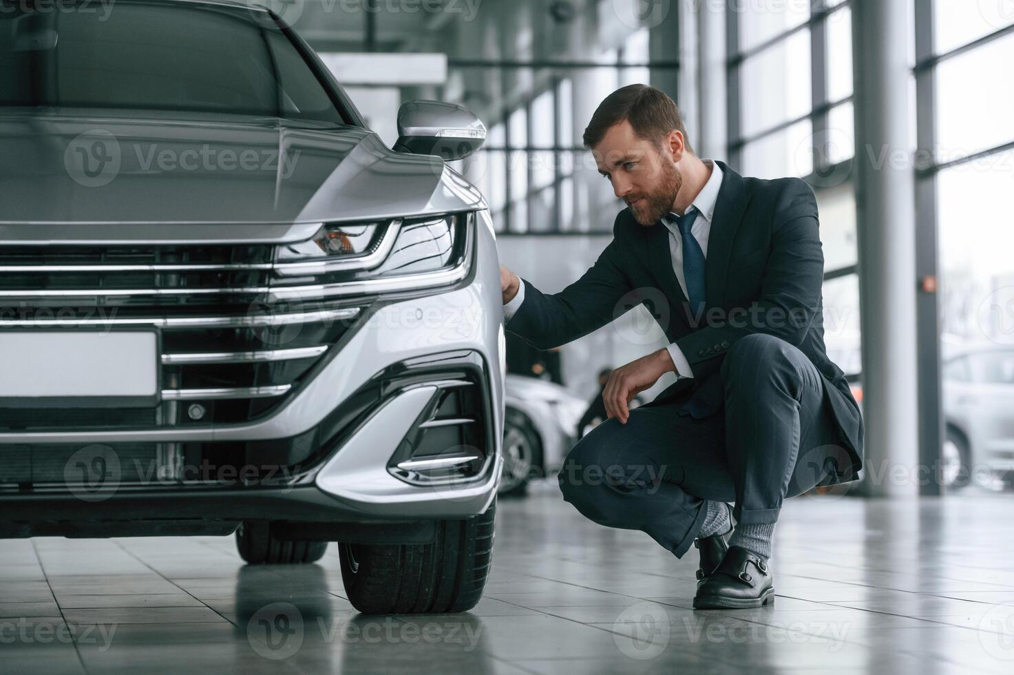 Man in suit and tie is sitting and checking, quality of the vehicle in the car showroom photo