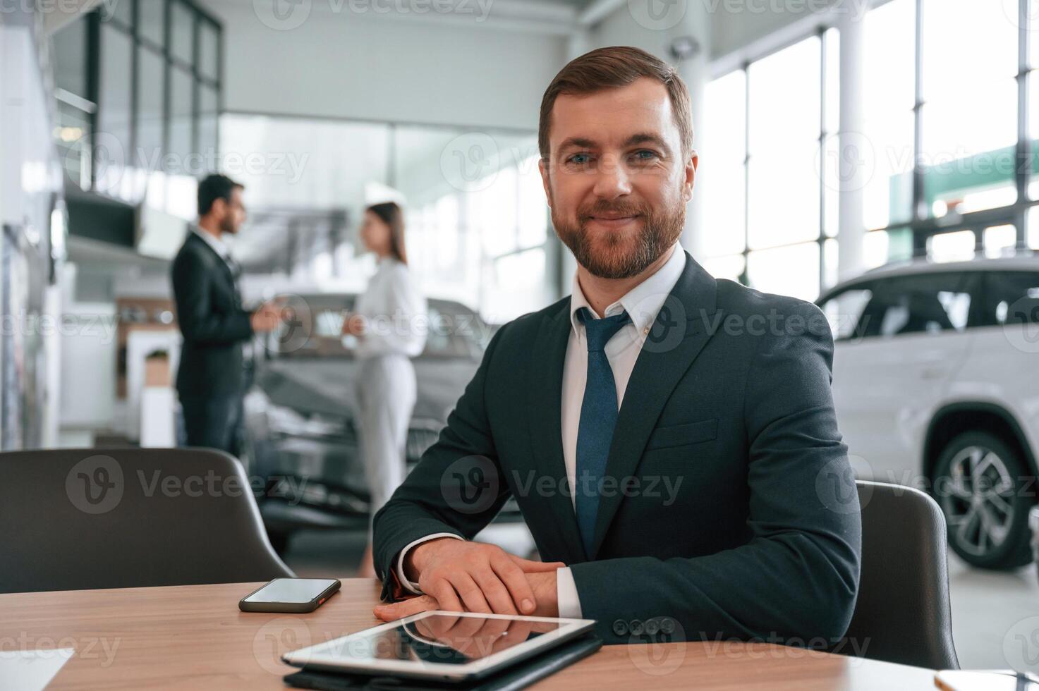 Man in ,headphones is, sitting by table. Three people are working together in the car showroom photo