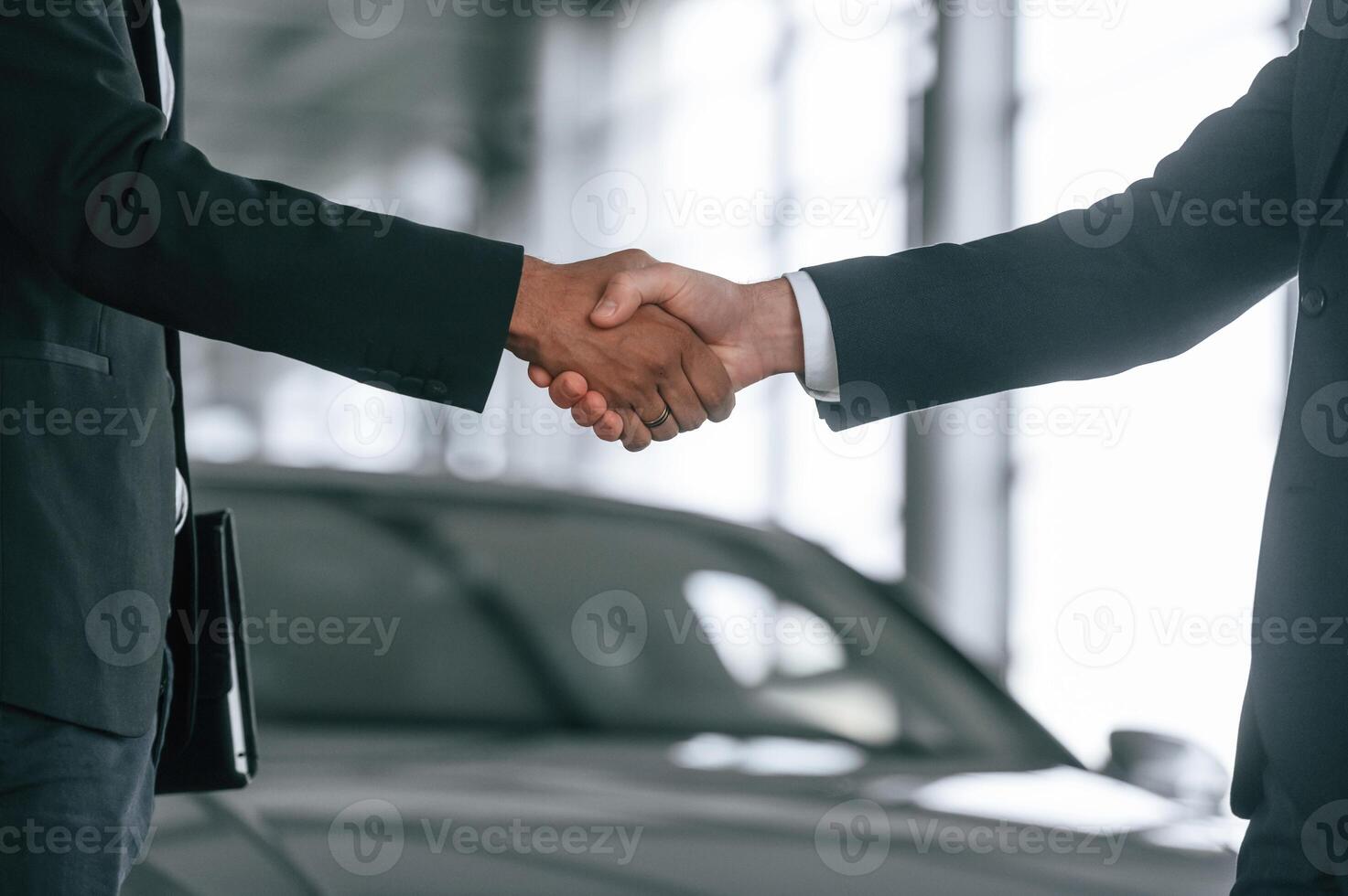 Close up view. Two, businessmen are standing, in the car showroom and making a deal, handshake photo
