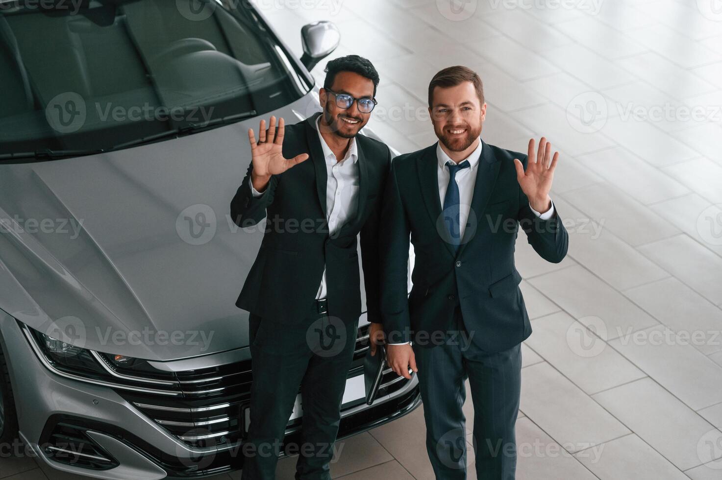 Near grey colored automobile. Two businessmen a,re working together in the car showroom photo