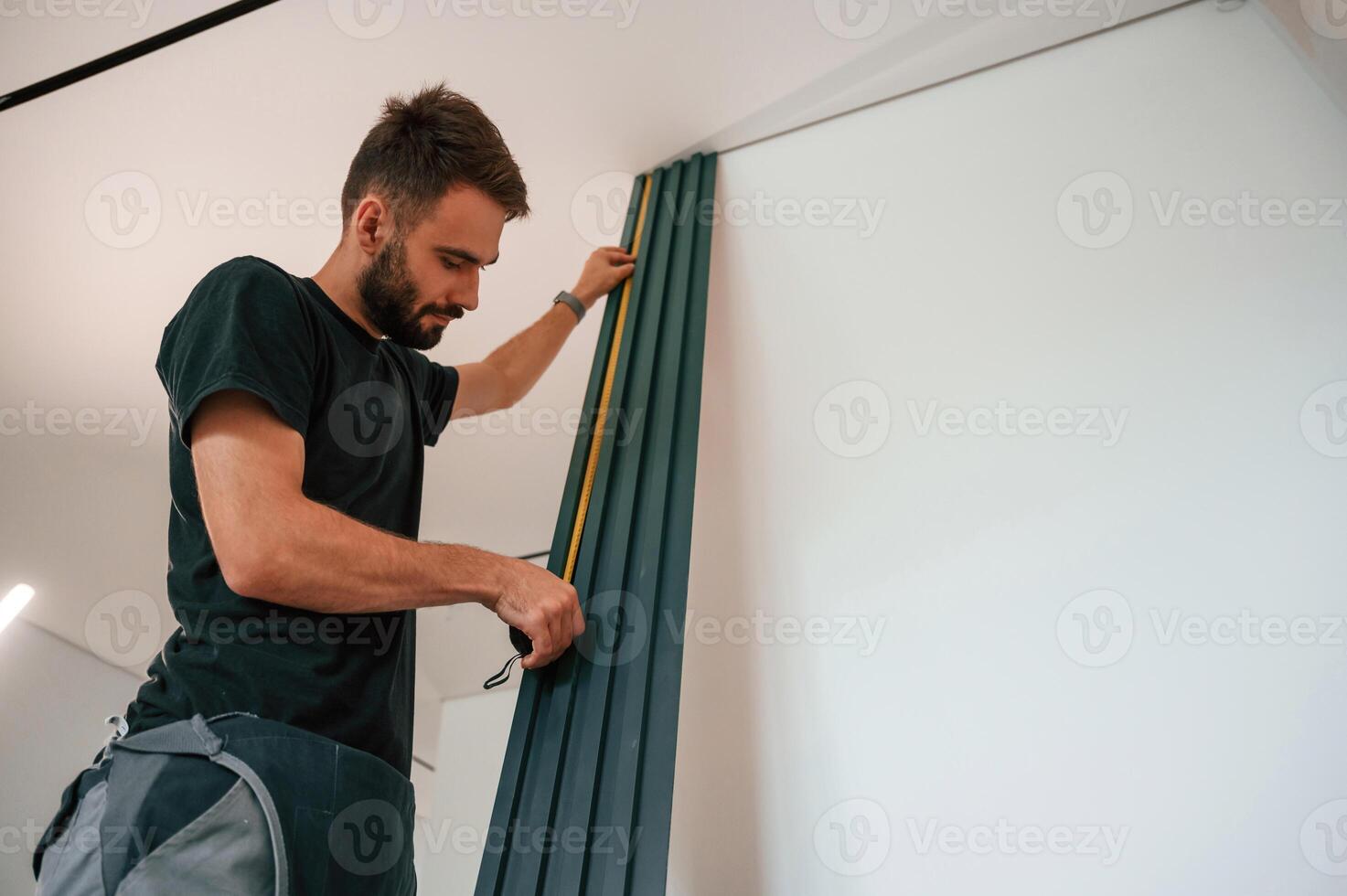 Taking, measurements. Plumber, worker installing heating radiator in empty room of a newly built house photo