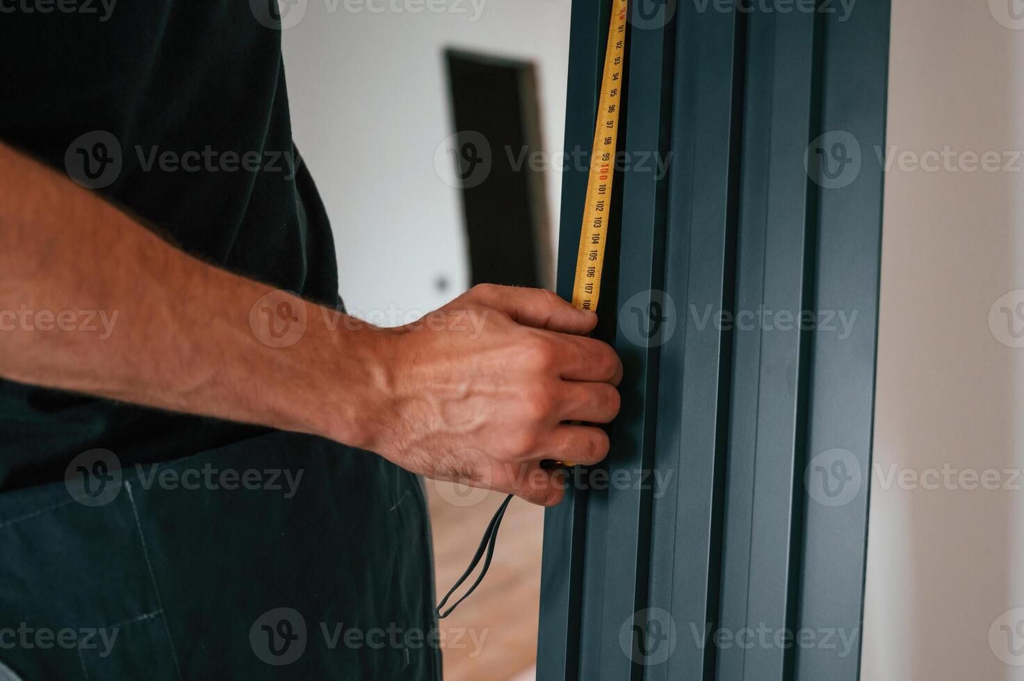 Taking measurements. Plumber worker installing heating radiator in empty room of a newly built house photo