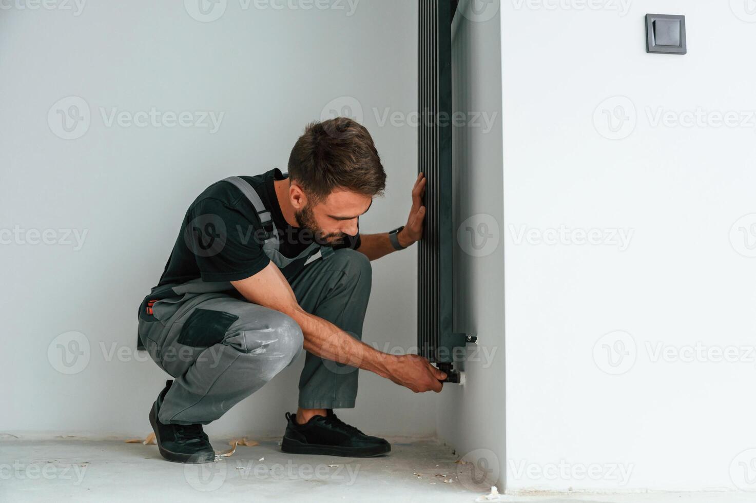 Plumber worker ,installing heating radiator in empty room of a newly built house photo