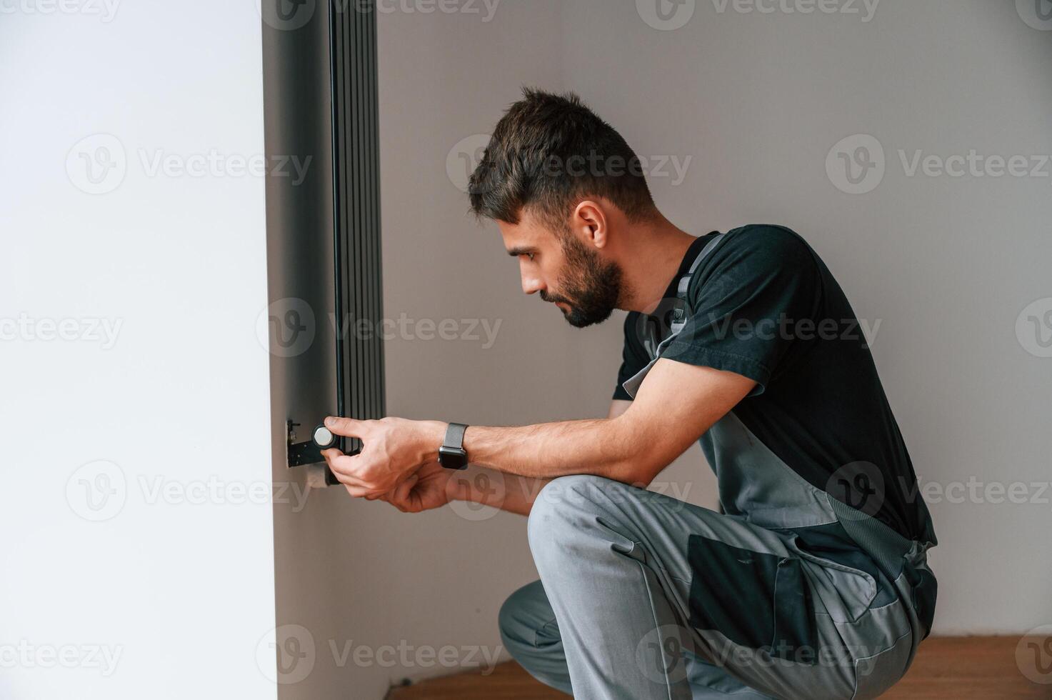 Plumber, worker ,installing heating radiator in empty room of a newly built house photo