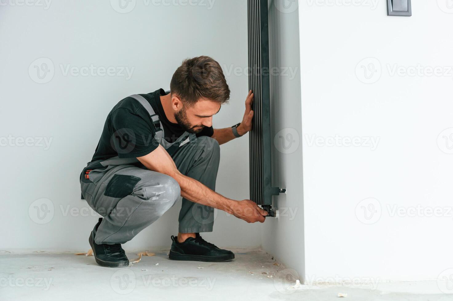 Plumber worker, installing heating radiator in empty room of a newly built house photo