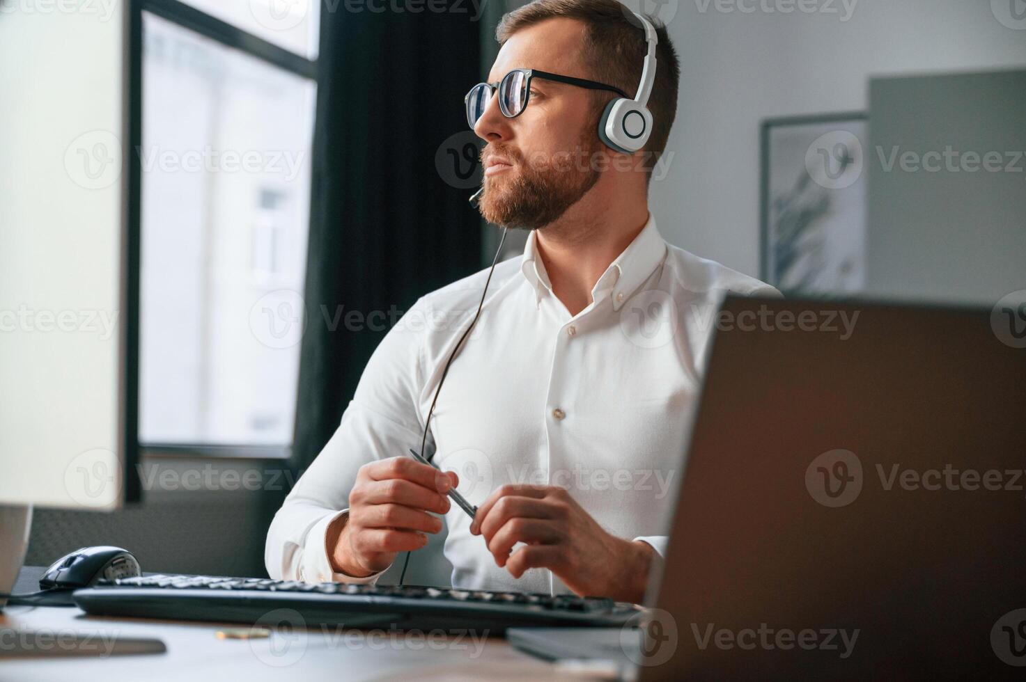 In headphones.. Man in formal clothes is working in the modern office. Using computer photo
