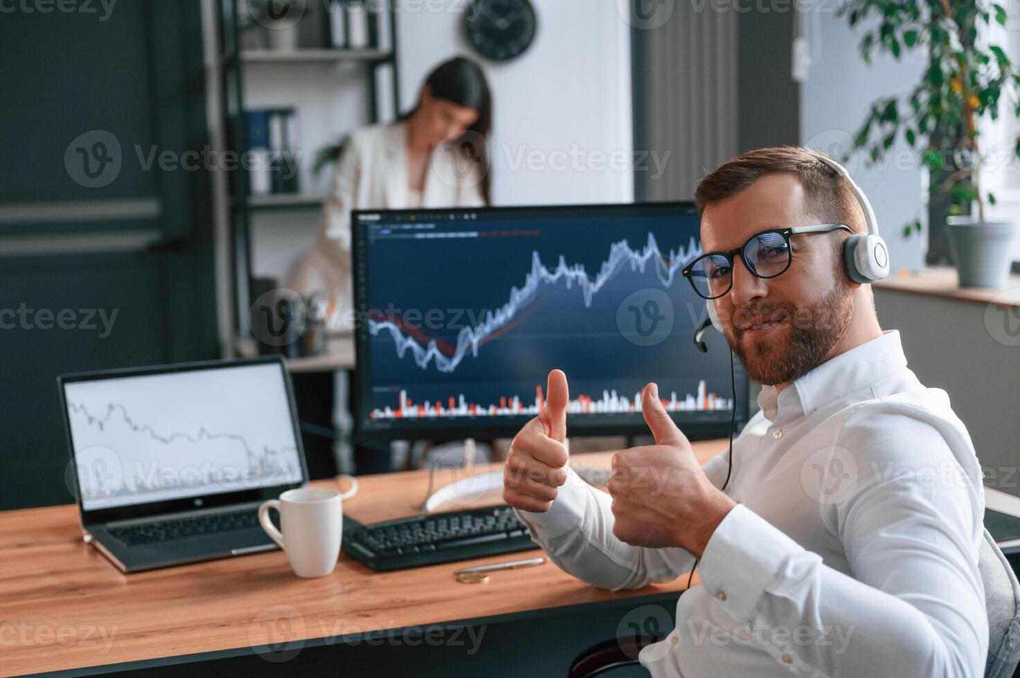 Man ,showing thumbs up. Graphs on the screen. Two employees are working together in the modern office photo