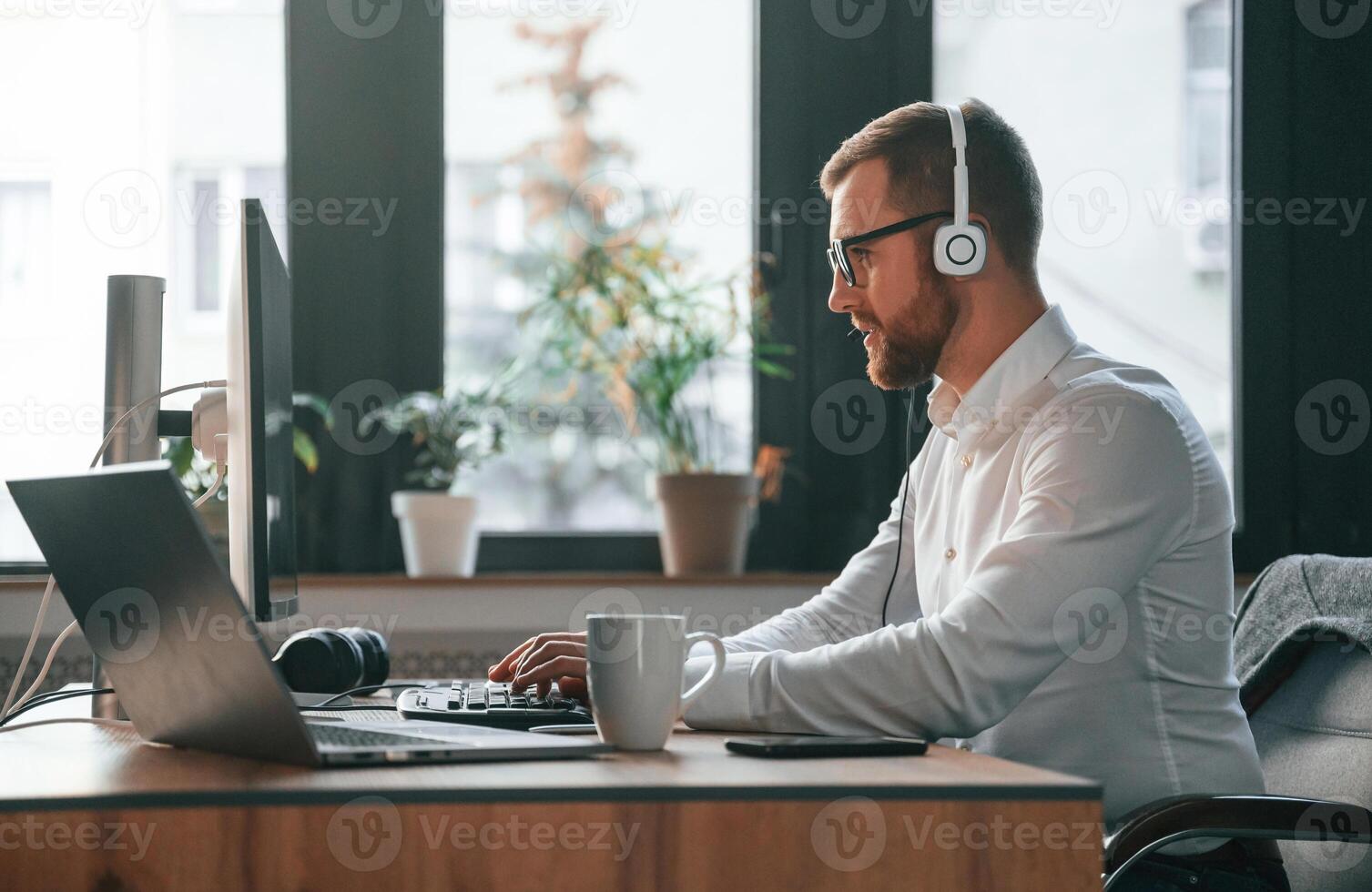 In the call ,center. Wearing headphones. Office worker in formal clothes is sitting by computer and working photo