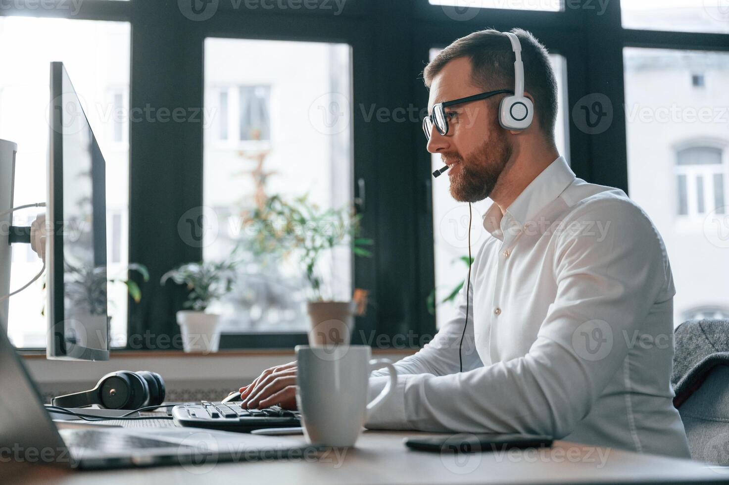 In the call center.. Wearing headphones. Office worker in formal clothes is sitting by computer and working photo