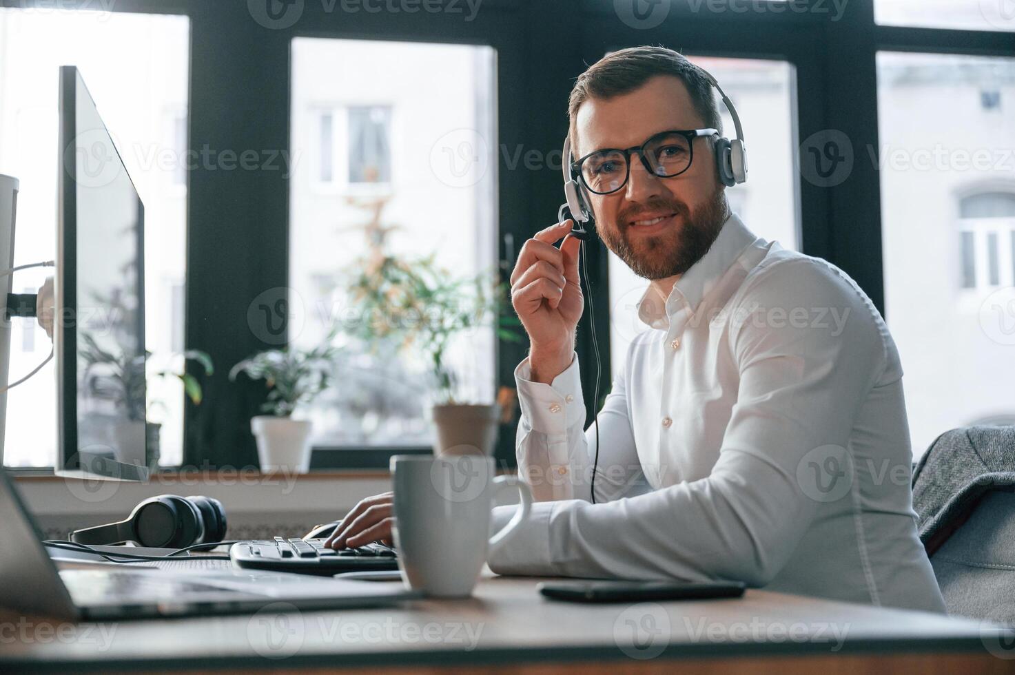 In the call center.. Wearing headphones. .Office worker in formal clothes is sitting by computer and working photo