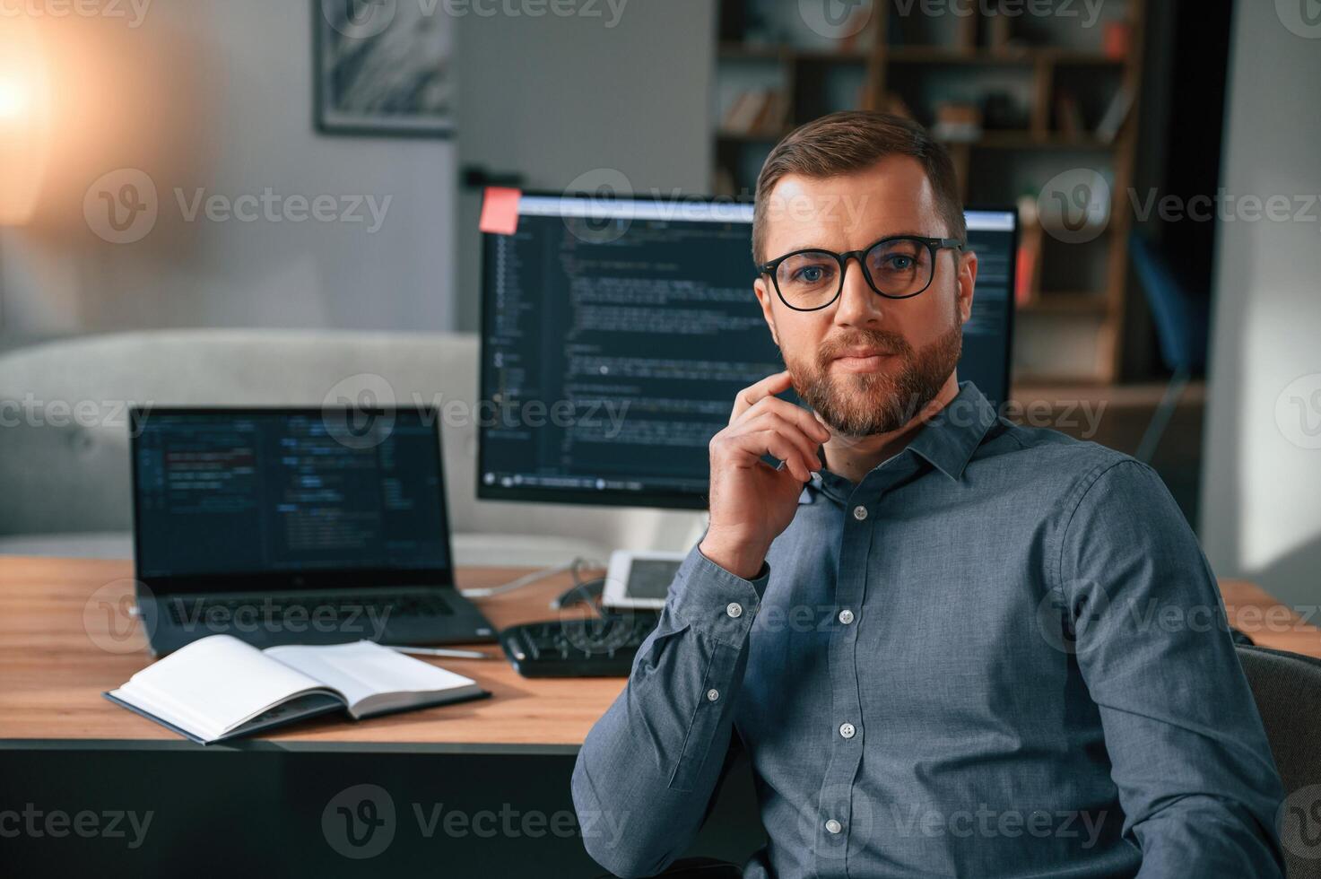 Software, developer is sitting, and posing. Man in formal clothes is working in the modern office. Using computer photo