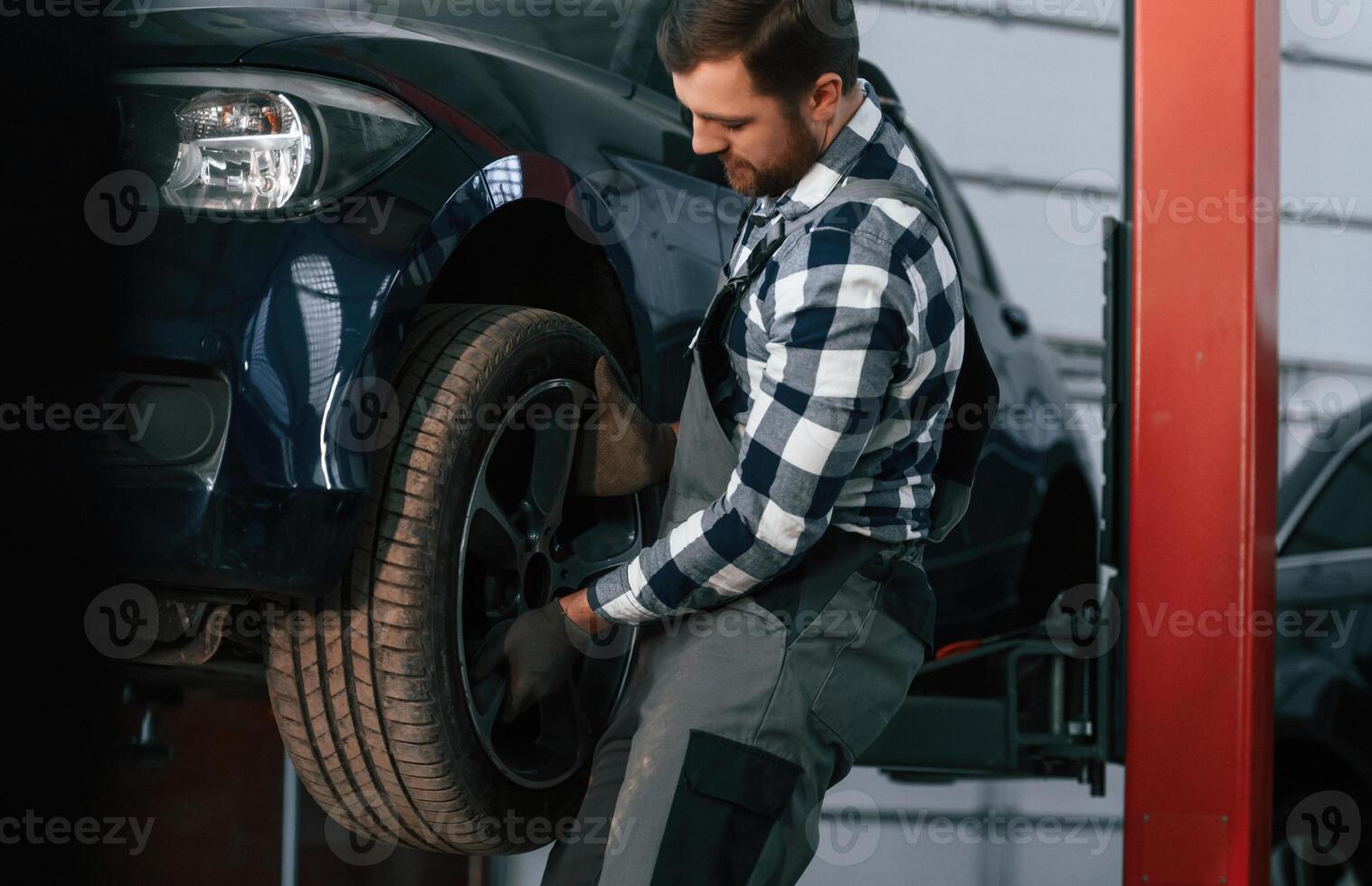 Holding, and ,changing ,new tire. Man in uniform is working in the auto salon photo