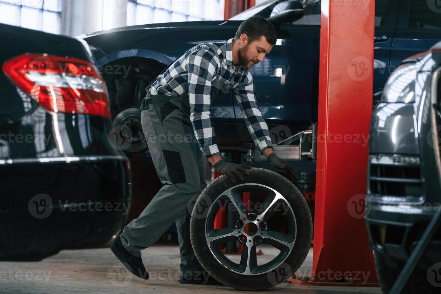 Side view.. Moving, the tire for the car. Man in uniform is working in the auto salon photo