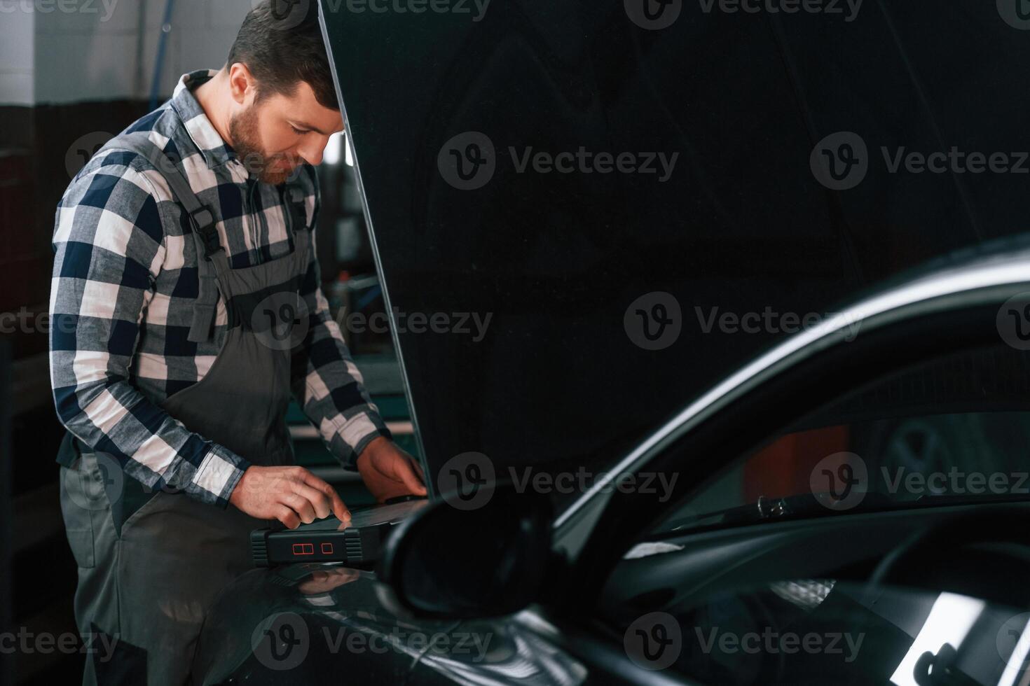 Black ,car is repairing. Hood is opened. Man in uniform is working in the auto salon photo