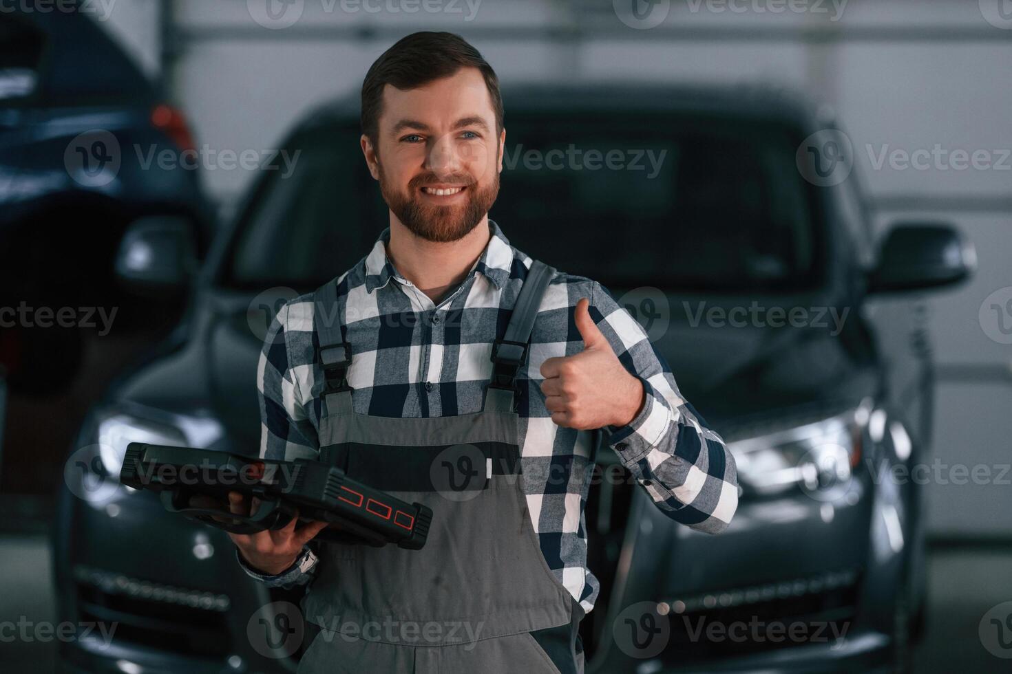 Showing, gesture and smiling. Holding tablet. Man in uniform is working in the auto salon photo