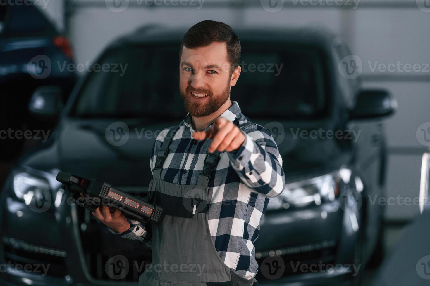 Showing gesture ,and smiling. Holding tablet. Man in uniform is working in the auto salon photo