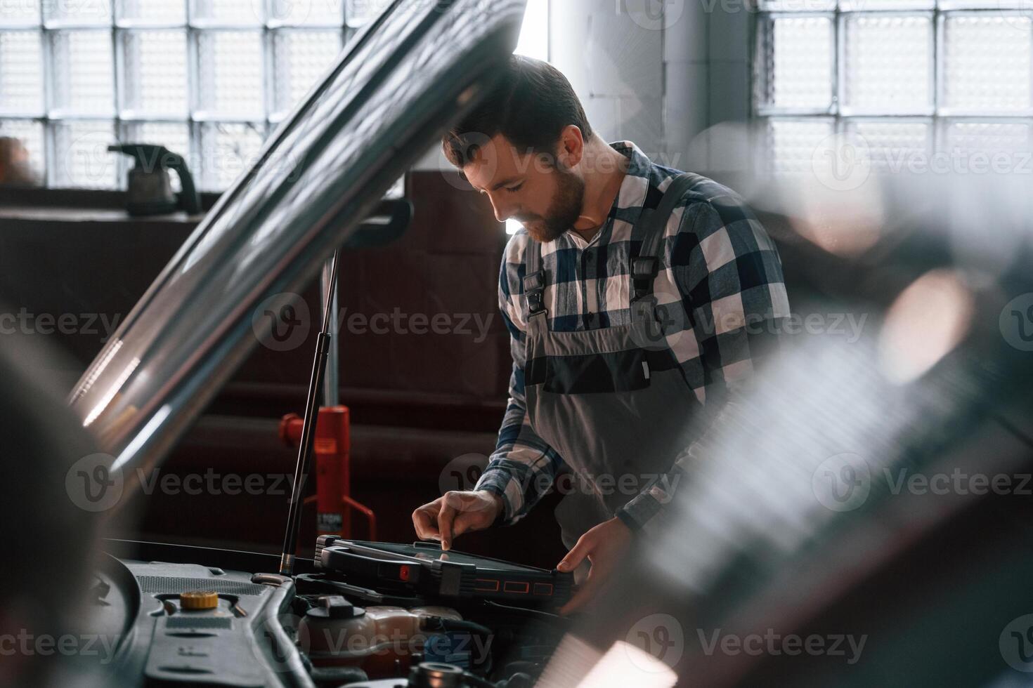 Hood ,of, the car is opened. Using tablet. Man in uniform is working in the auto salon photo